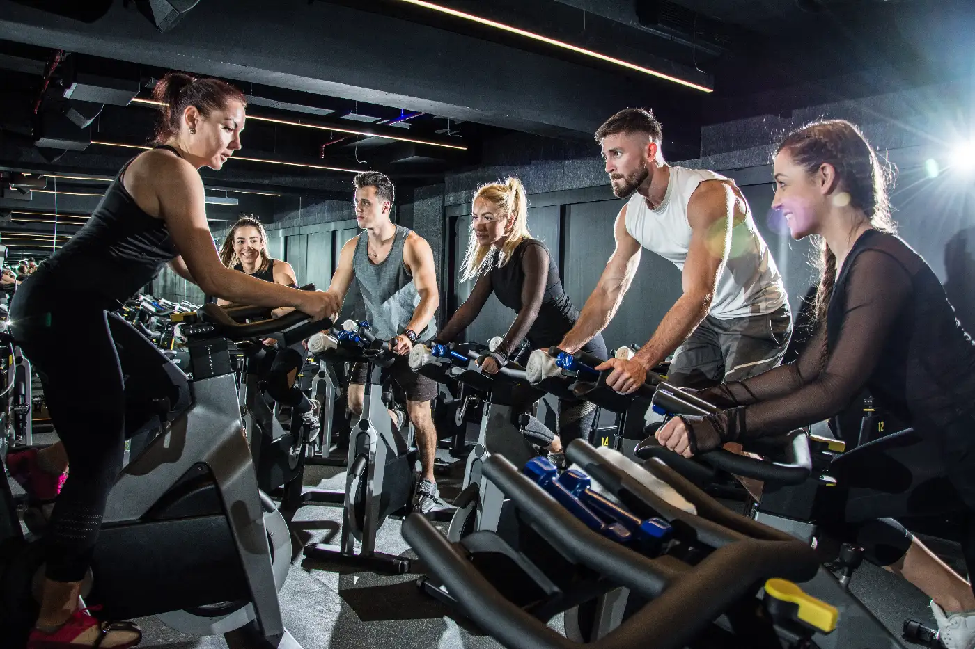 Group of young adults taking part in a spinning class in a dark gym