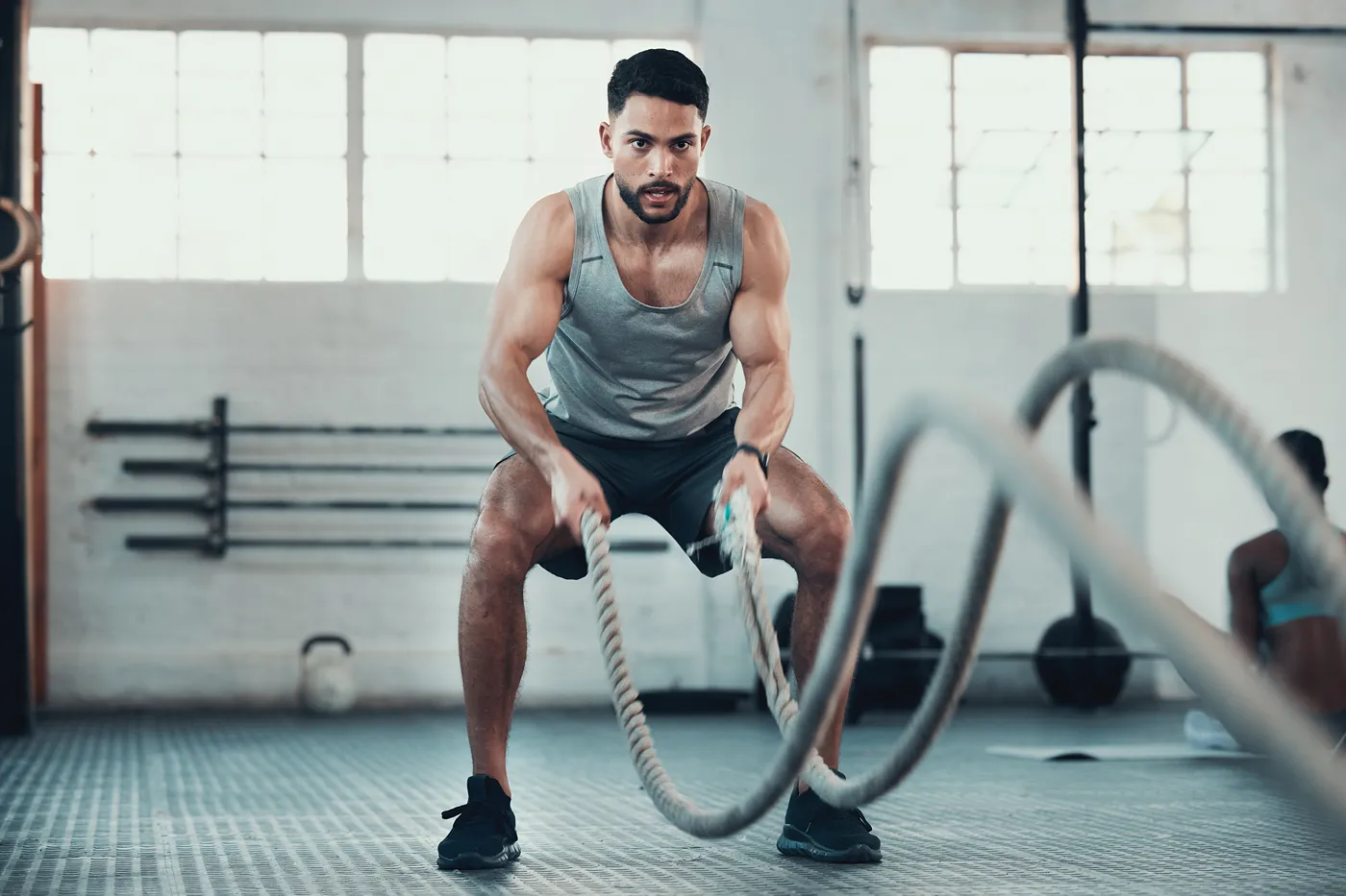 Man with intense look on his face in gym using battle ropes to workout