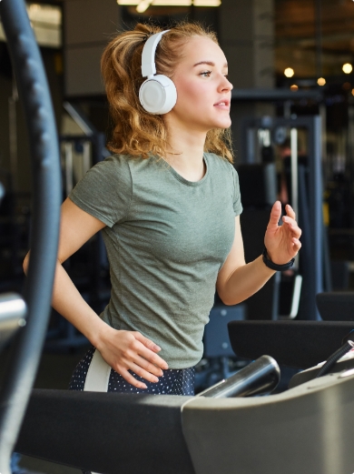 A young woman with headphones on using a treadmill in a gym
