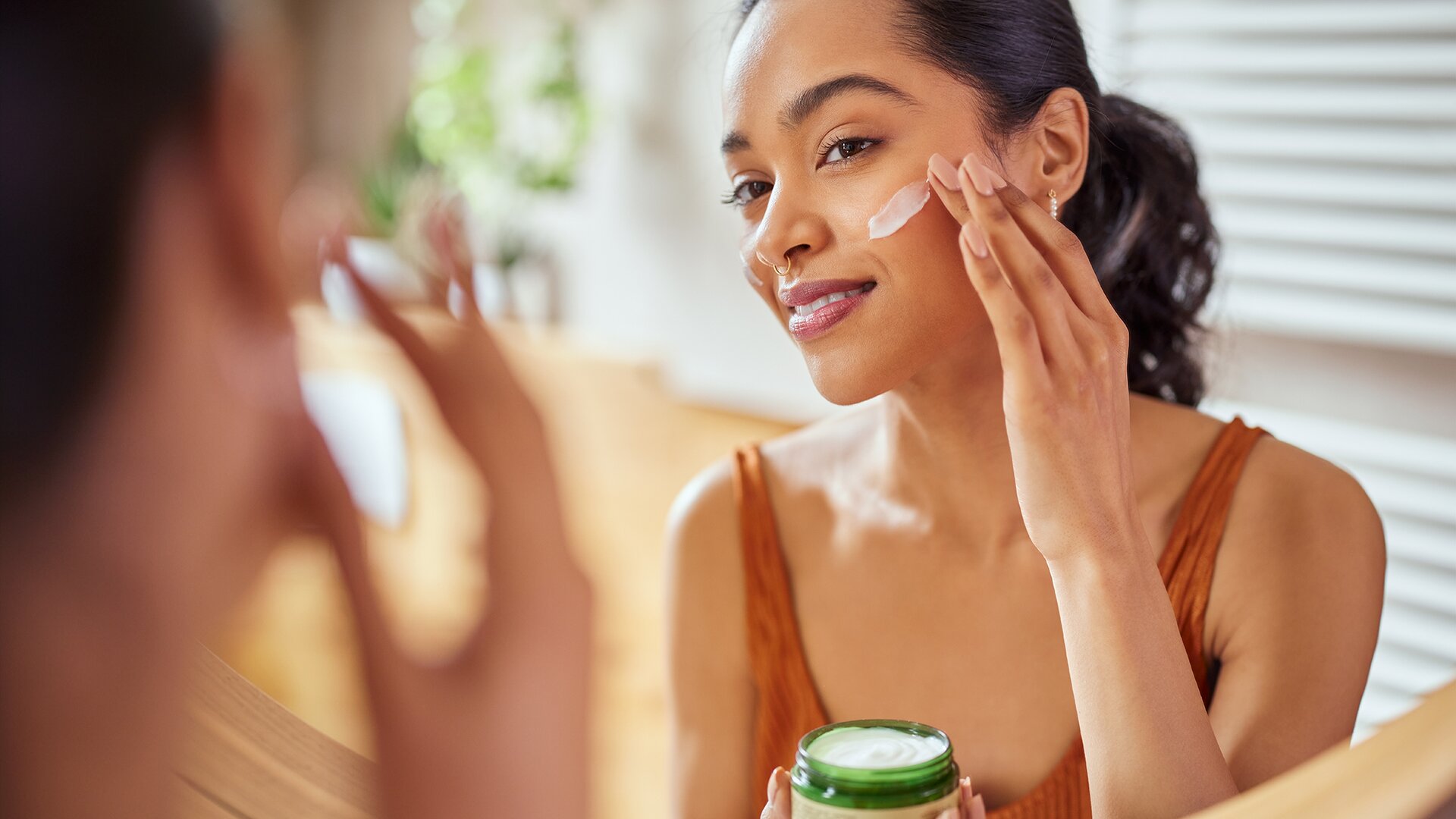 A smiling woman looking in the mirror applying face cream