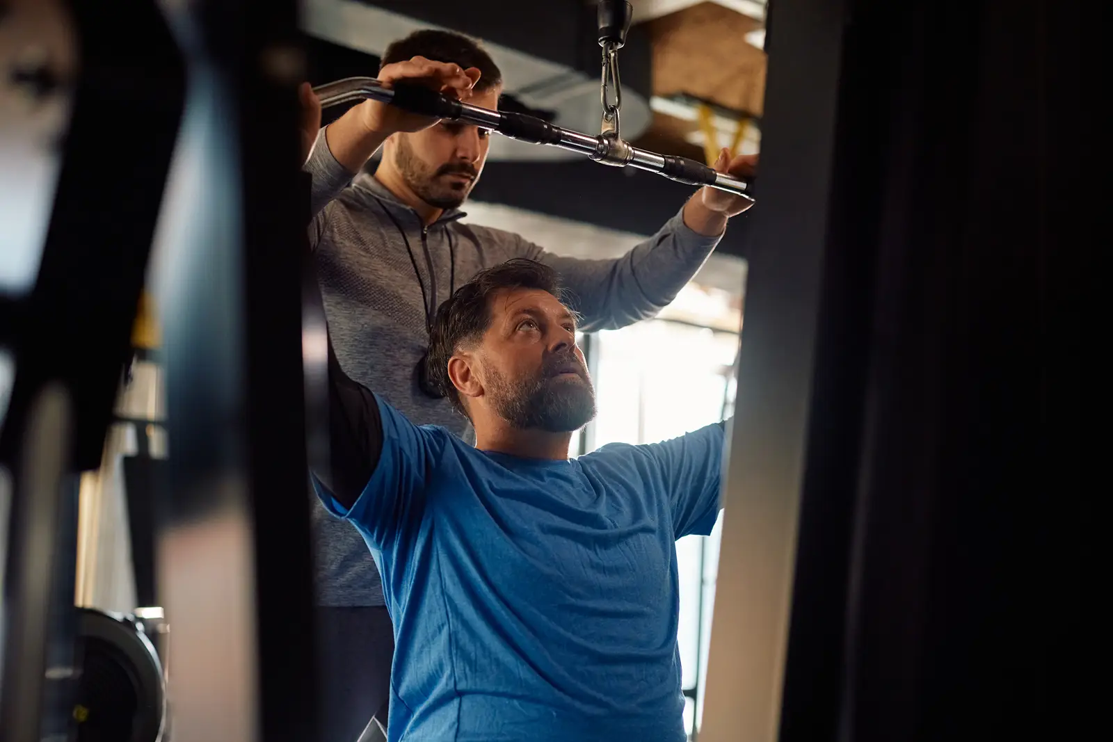 A man using a resistance weight machine and being helped by a personal trainer